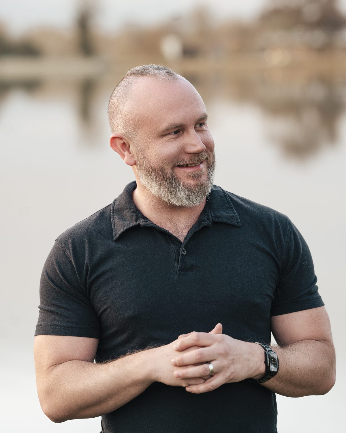 Johnny in a black polo by a lake, smiling and looking off to the side.