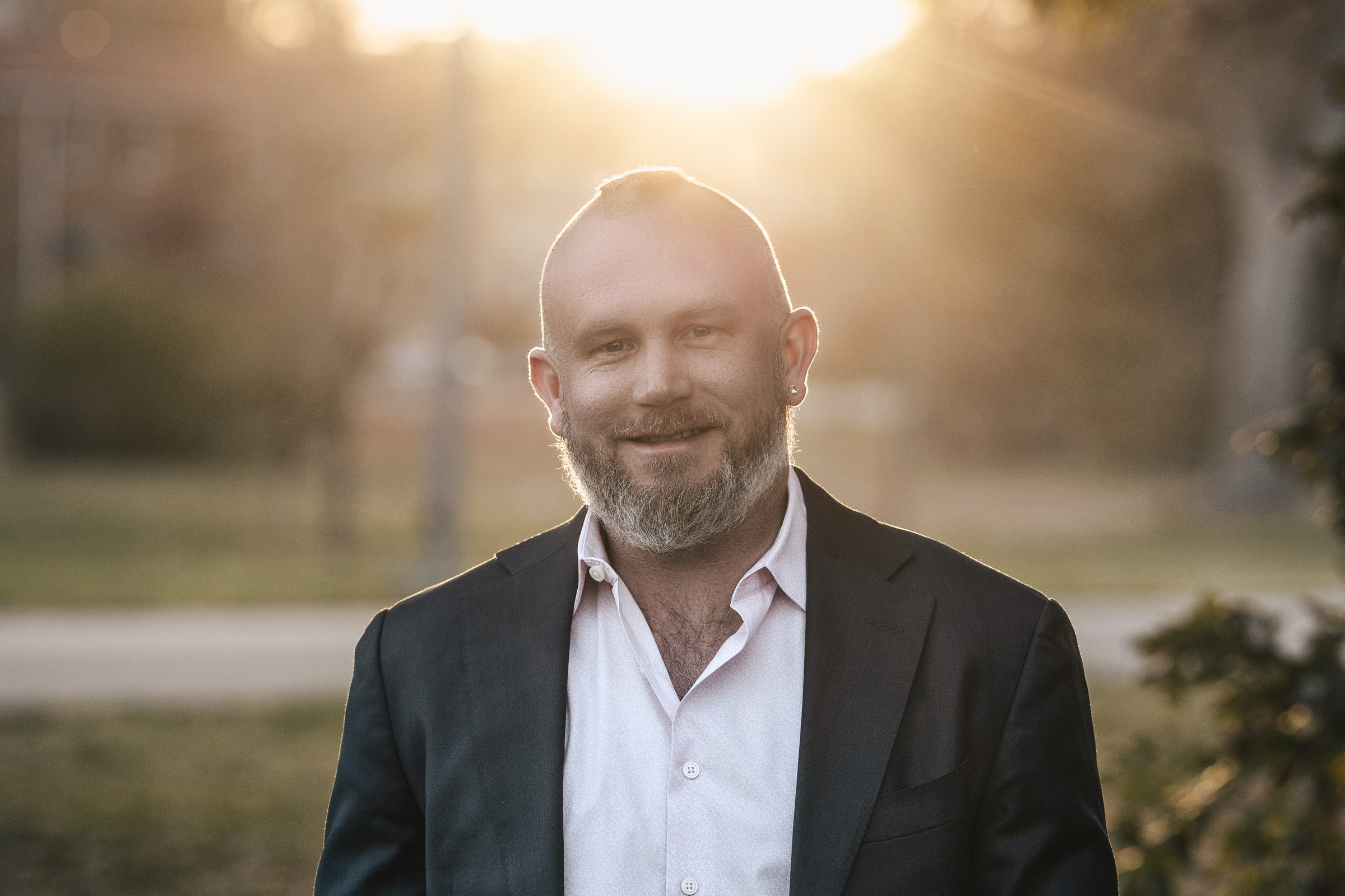 Johnny Fermin-Robbins in a dark blazer, standing in a park at golden hour.