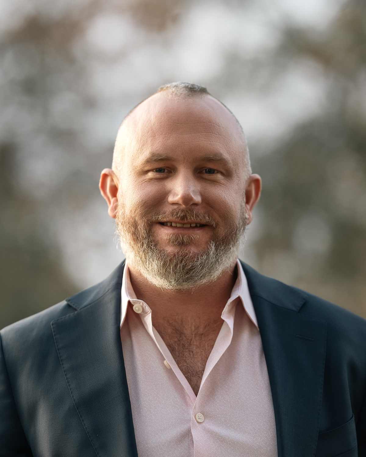 Portrait of Johnny in a dark blazer and pale pink shirt, smiling.